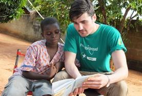 Sociale zorg Jongerenreizen:Een vrijwilliger in Togo helpt een scholier bij het lezen van een Engelstalig boek tijdens de groepsreis voor jongeren. Een vrijwilliger in Togo helpt een scholier bij het lezen van een Engelstalig boek tijdens de groepsreis voor jongeren.