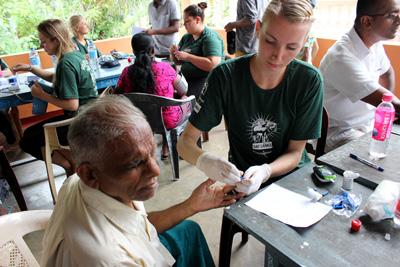 Vrijwilligers doen verschillende medische controles zoals het meten van de bloeddruk en de bloedsuikerwaarden Projects Abroad vrijwilliger test de bloedsuikerwaarden en bloeddruk tijdens een outreach in Sri Lanka